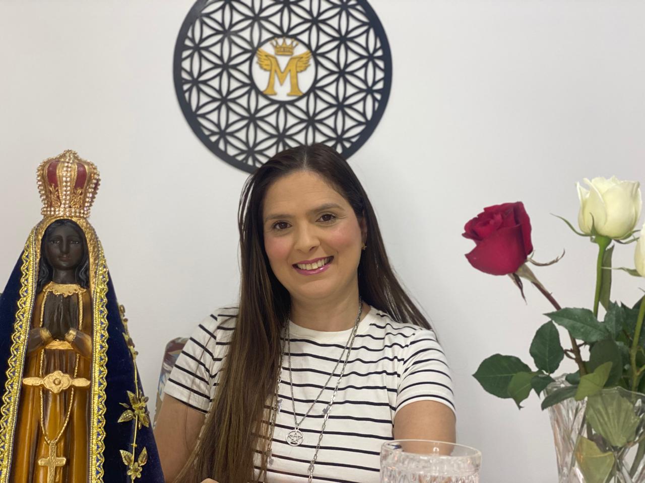 Terapeuta sorrindo em seu espaço de atendimento com flores e imagem sagrada